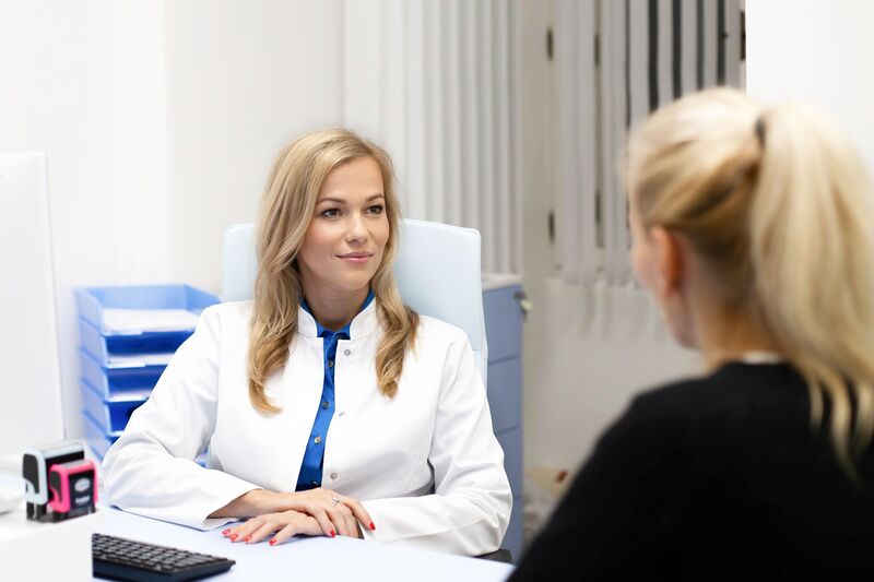 Blonde cardiologist in a white coat consulting with a patient across her desk in a bright clinic