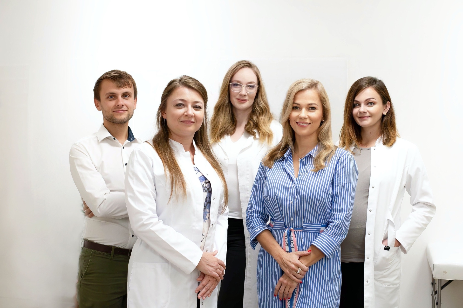 Group portrait of a five-member cardiology team in white coats and shirts against a bright white wall