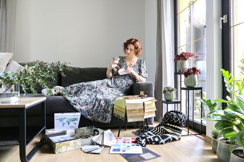 Interior designer in a floral dress on a grey sofa studying fabric and colour samples surrounded by plants