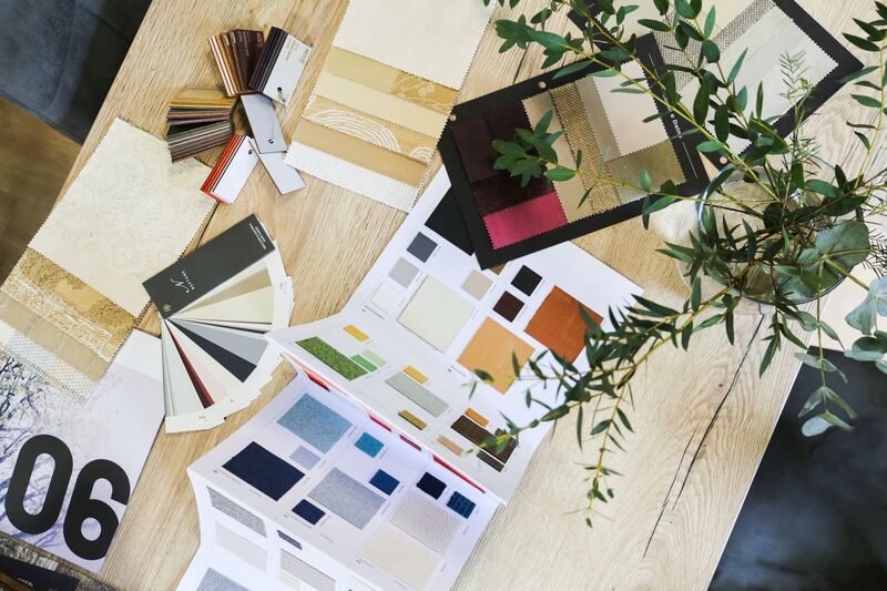 Overhead flatlay of fabric, leather and colour swatches on a wooden table with eucalyptus branches