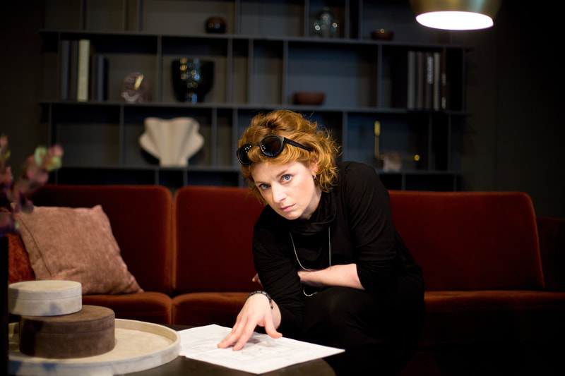 Red-haired designer in black with sunglasses on her head leaning over blueprints on a coffee table