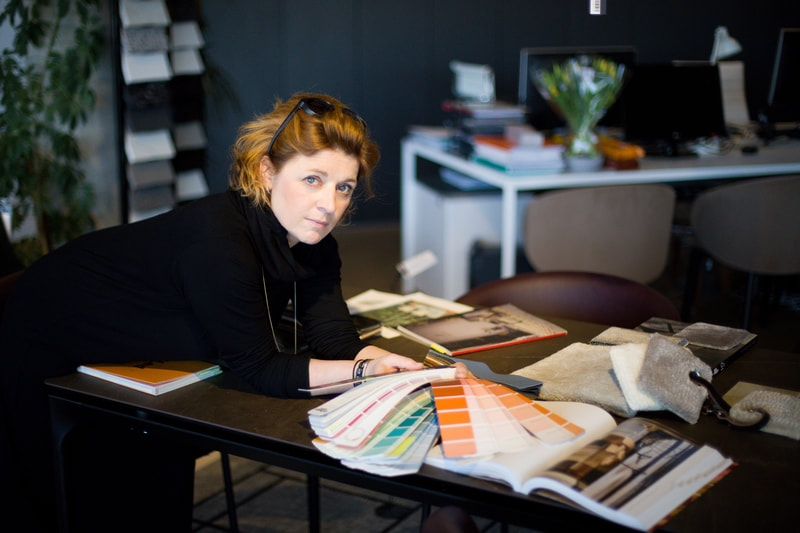 Red-haired designer in a black turtleneck reviewing orange and pastel colour swatches at her studio desk