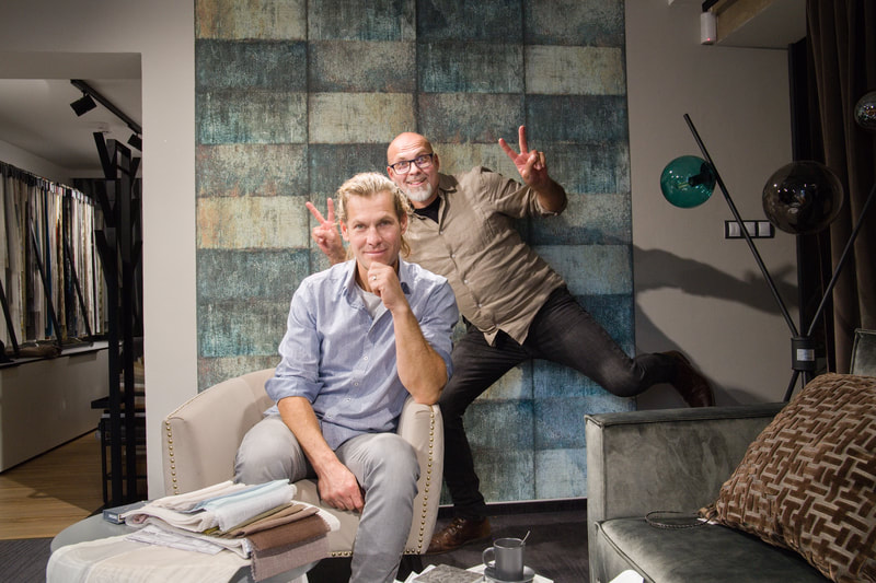 Two men flashing peace signs in an interior design showroom with a textured blue fabric wall